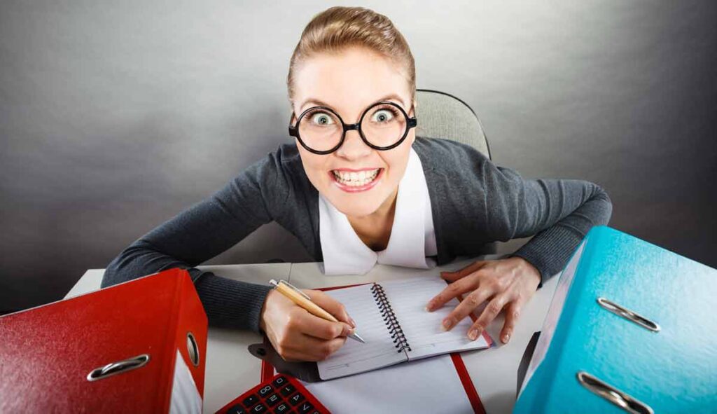 Eine Frau mit großer Brille schaut aggressiv von Akten hervor. (c) AdobeStock