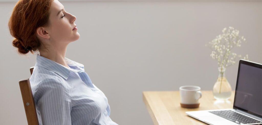 Eine Frau sitzt mit geschlossenen Augen auf einem Sessel vor einem Laptop. (c) AdobeStock