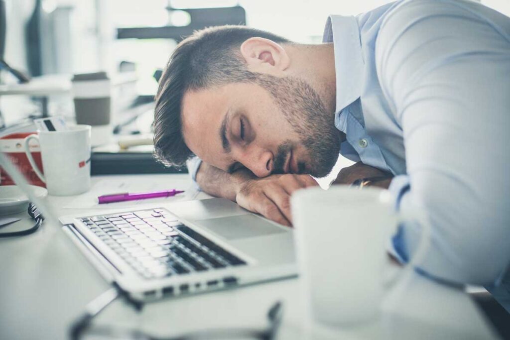 Ein Mann, der auf seinem Schreibtisch auf seinem Laptop schläft. (c) AdobeStock