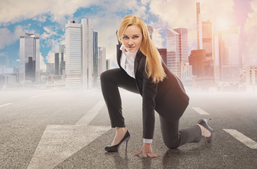 Illustration: eine Frau in Business-Anzug kniet in Position zum Losrennen; dahinter die Skyline einer Stadt. (c) AdobeStock