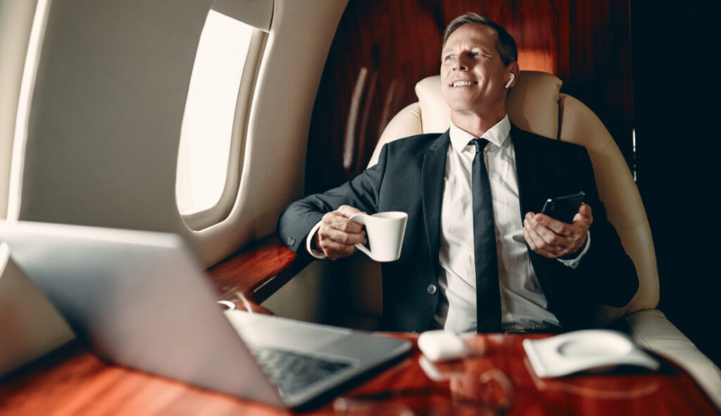 Senior businessman in suit flying in private jet and listening to music via wireless earphones. (c) AdobeStock