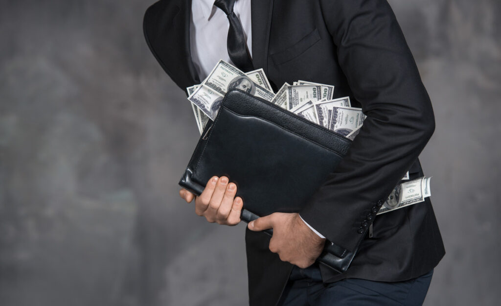 Ein Mann, der eine Tasche voller Geld fest hält. (c) AdobeStock