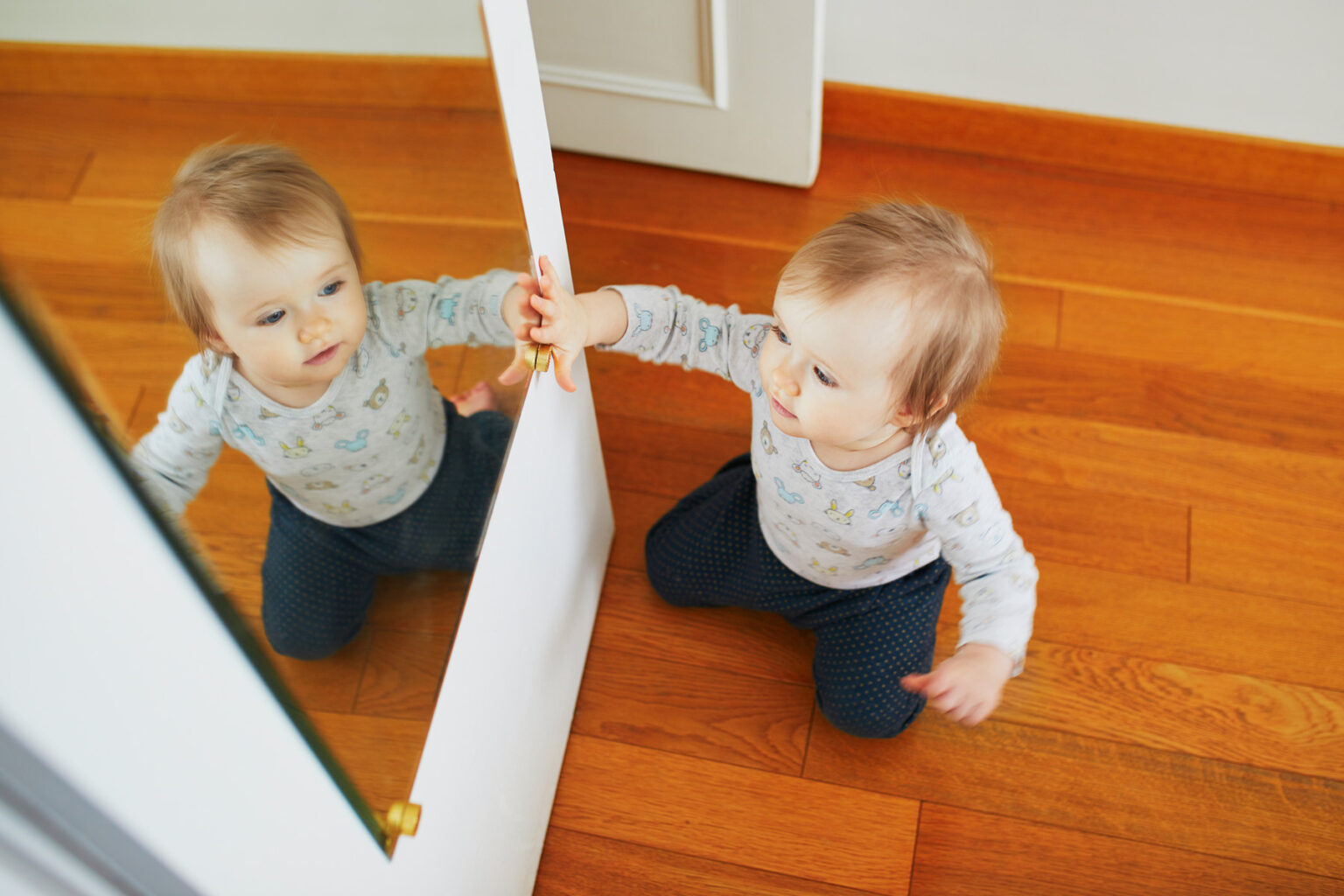 Baby girl playing with her reflection in mirror. Happy healthy little child at home. (c) AdobeStock