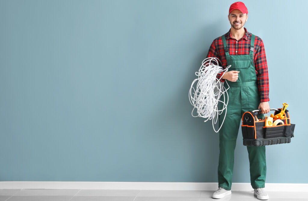 Male electrician with tools kit near color wall. (c) AdobeStock