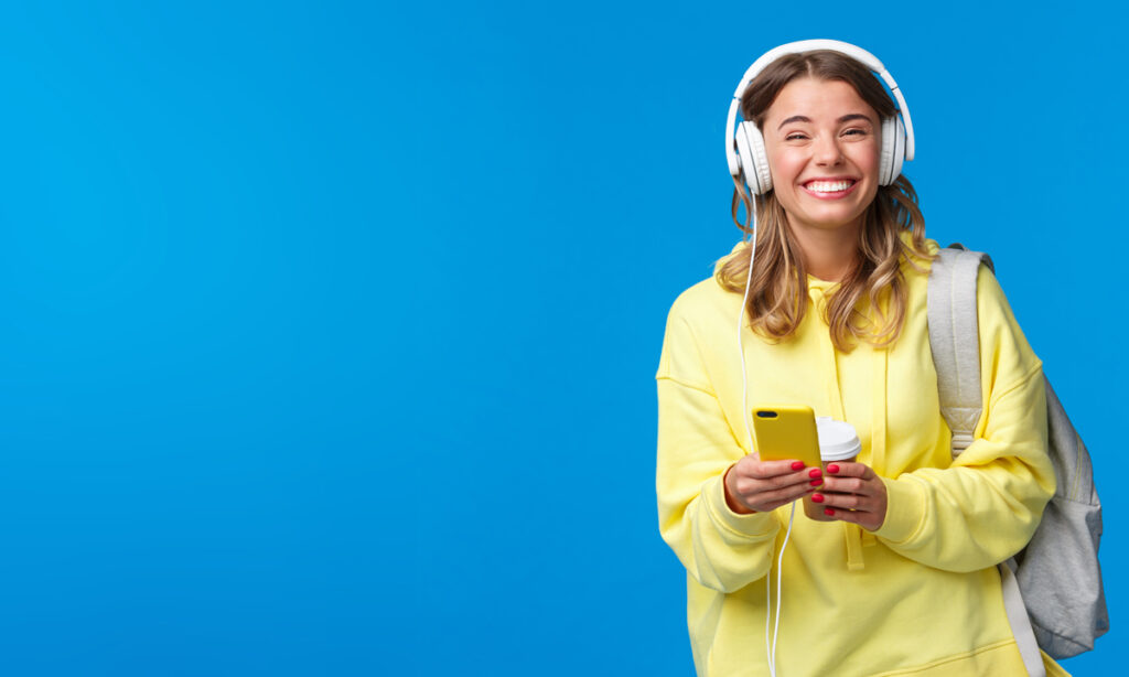 Umfrage enthüllt: 98,2 % der Menschen glauben, dass sie die lustigste Person sind, die sie kennen. 1 Cheerful pretty young female student with backpack, listening favorite playlist in headphones, laughing and smiling at camera carefree, hold mobile phone, stand blue background, Stichwort lustigste Person.
(c) AdobeStock