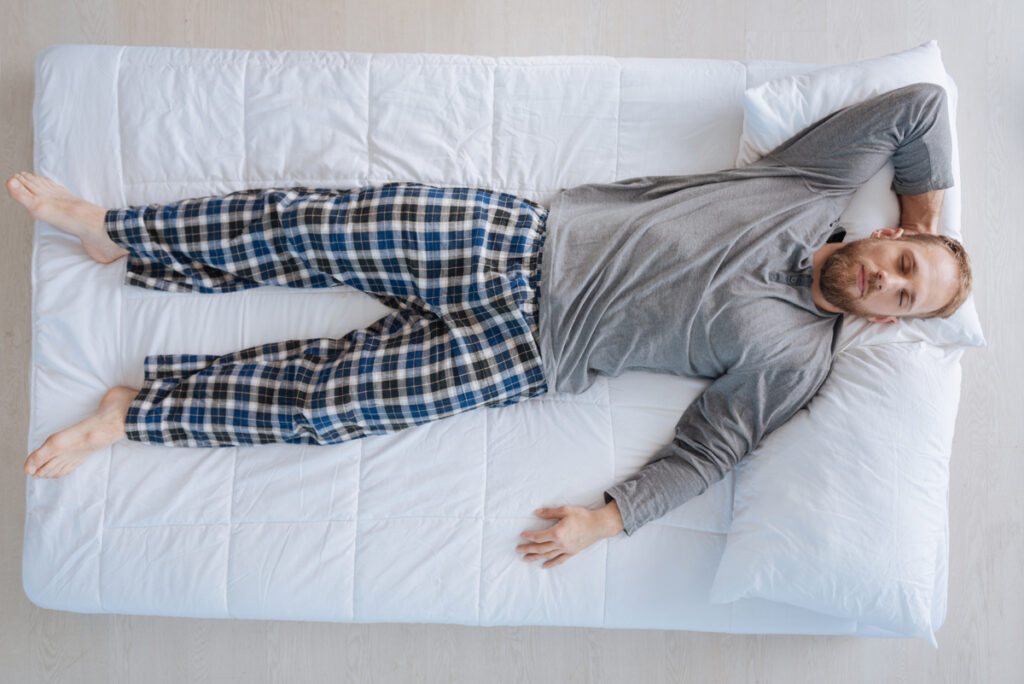Time to relax. Handsome peaceful bearded man lying on the bed and sleeping while resting at home. (c) AdobeStock