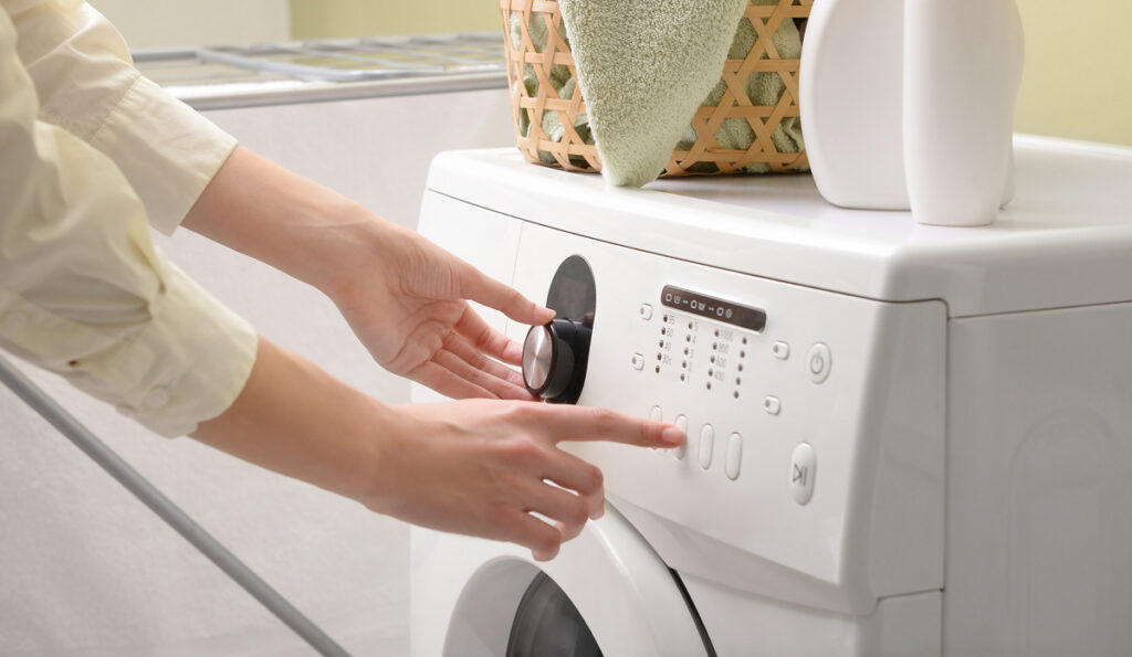 Woman switching on washing machine. (c) AdobeStock
