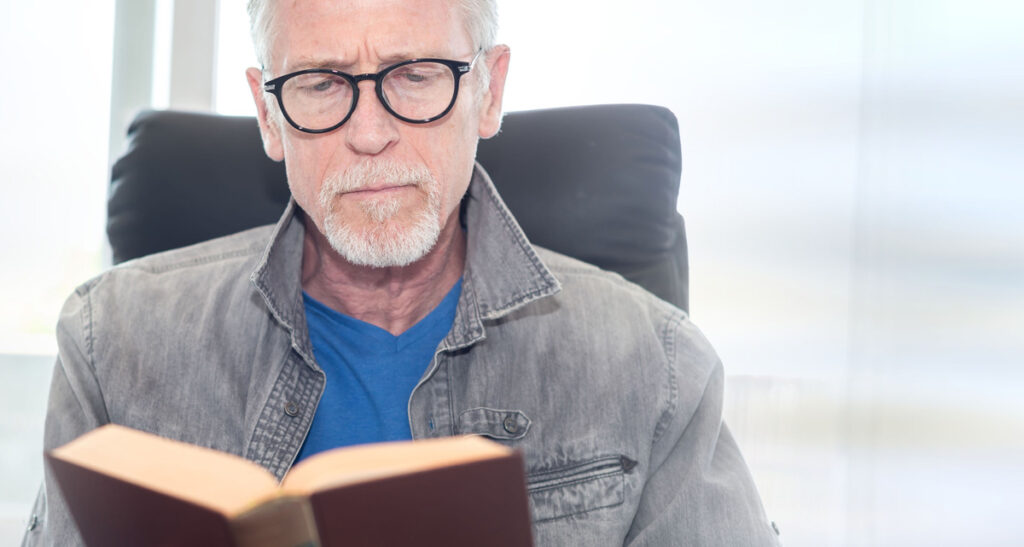 Portrait of mature man reading a book at home. (c) AdobeStock