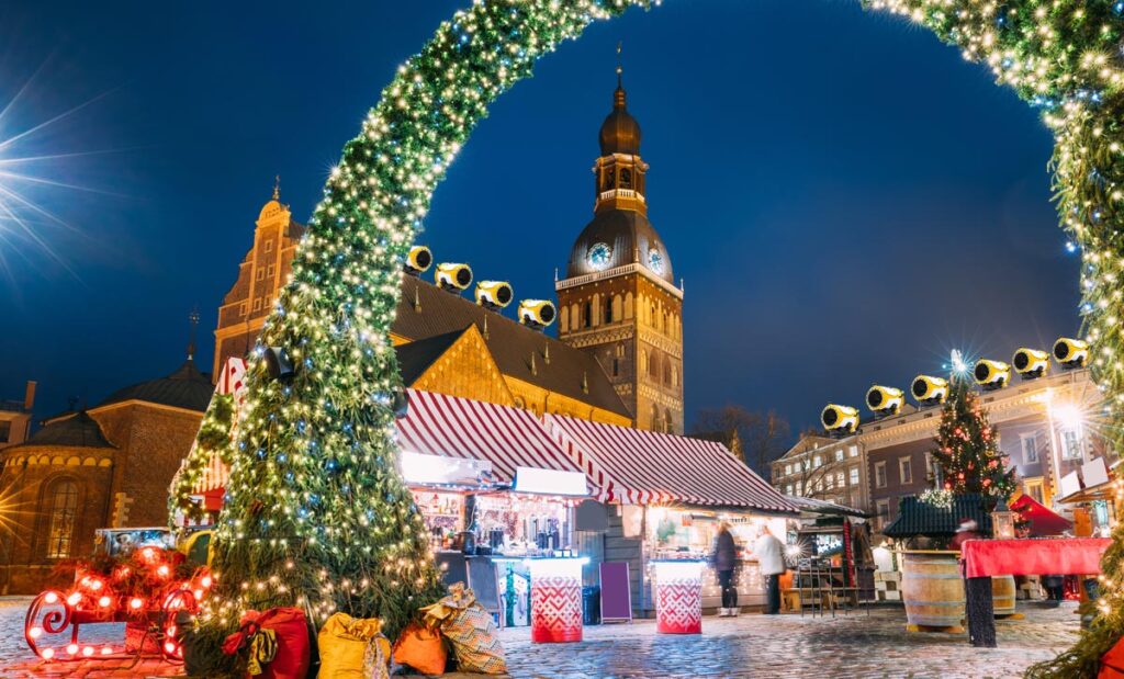 Riga, Latvia. Christmas Market On Dome Square With Riga Dome Cathedral. Christmas Tree And Trading Houses. Famous Landmark At Winter Xmas Evening Night In Illuminations Light. (c) AdobeStock/ K2