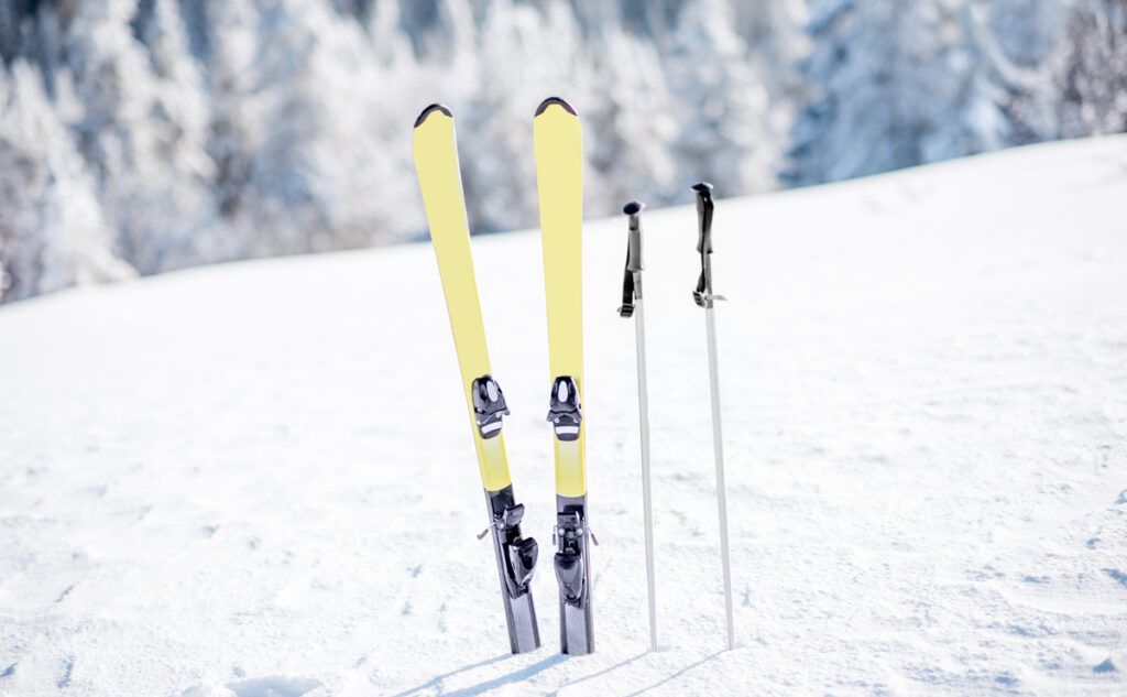 Skis with sticks on the snowy mountains with frozen forest on the background (c) AdobeStock