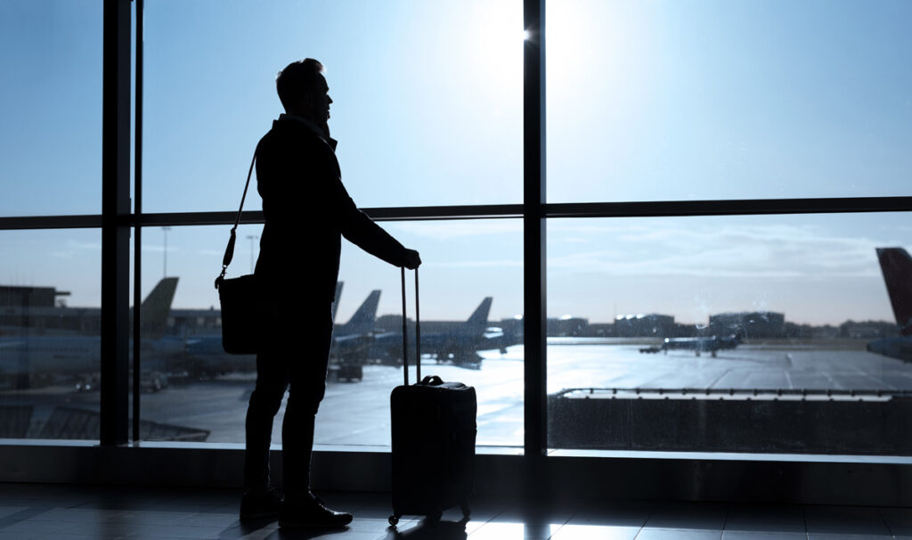 Ein telefonierender Mann auf einem Flughafen, der auf die Flugzeuge schaut. (c) AdobeStock