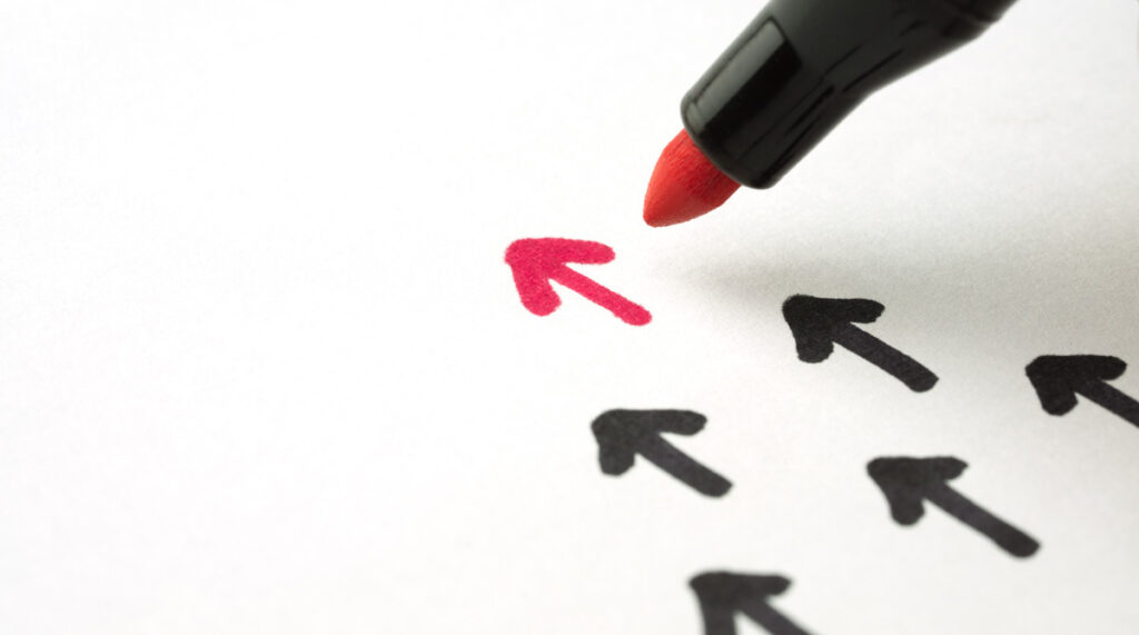 Die Spitze eines roten Filzstiftes, mit dem ein kleiner Pfeil vor anderen schwarzen gezeichnet wird. (c) AdobeStock