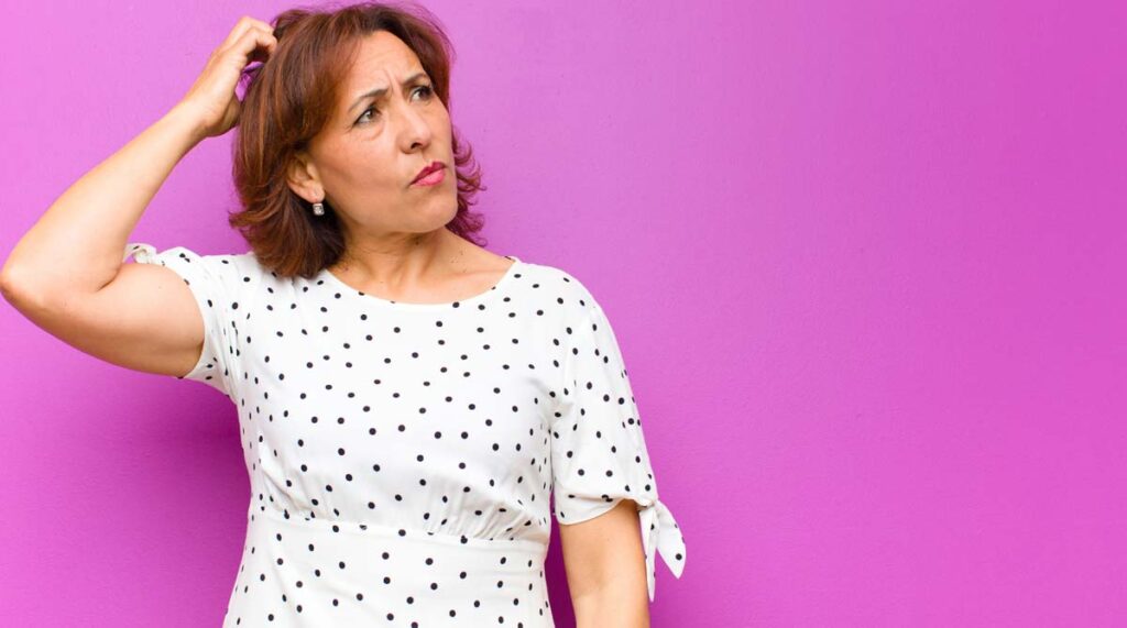 Eine ratlose Frau, die sich mit einer Hand am Kopf kratzt. (c) AdobeStock