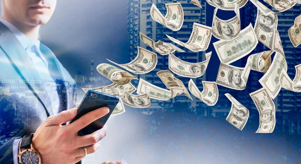 Die Hand eines Mannes, der ein Smartphone hält, aus dem Dollar-Scheine fliegen. (c) AdobeStock