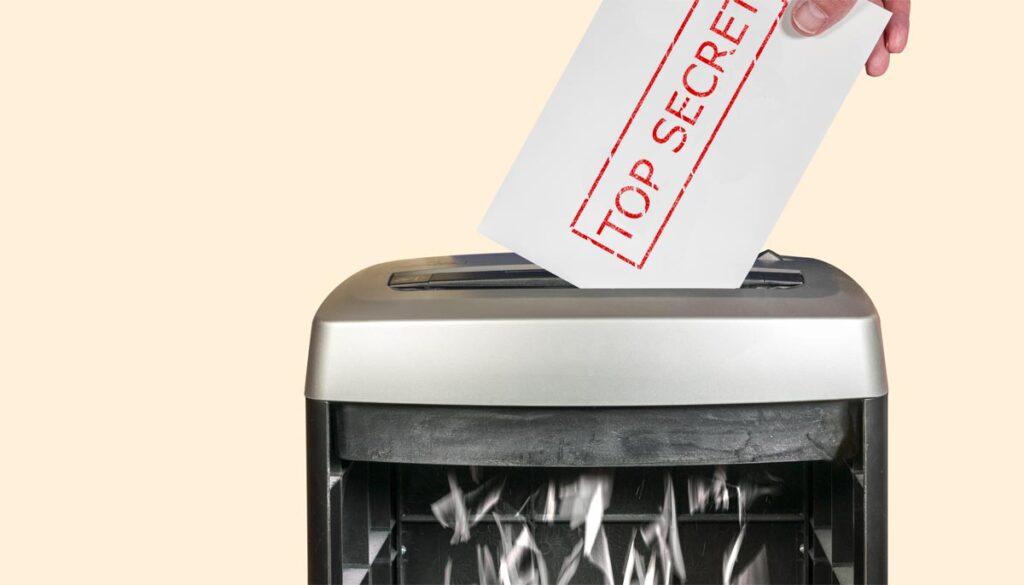 Die Hand eines Mannes, der ein Blatt mit "Top Secret" in einen Schredder steckt. (c) AdobeStock/ K2