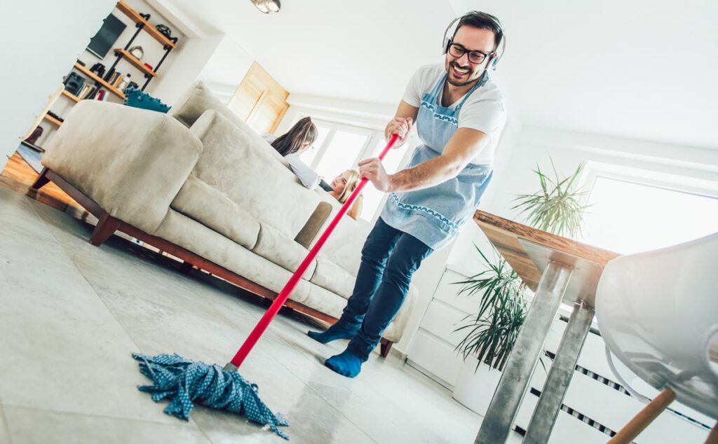 Ein Mann mit Brille und Kopfhörer beim Wischen des Bodens. (c) AdobeStock