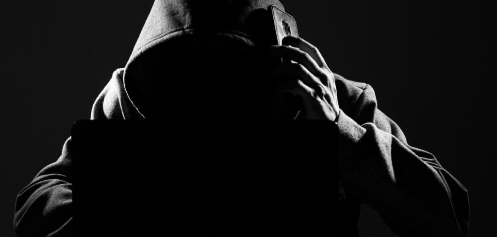 Ein Mann mit dunkler Kapuze über dem Kopf beim Telefonieren. (c) AdobeStock