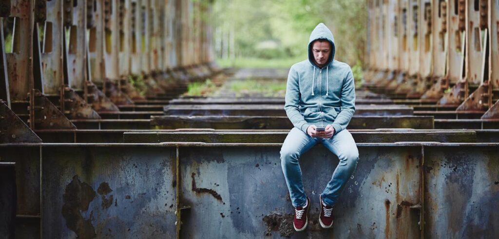 WhatsApp-Debakel: Mann wartet 8 Jahre auf eine Nachricht von seiner Geliebten Ein Mann mit Kapuzenpullover sitzt auf einem "lost place" und schaut traurig auf sein Handy. (c) AdobeStock