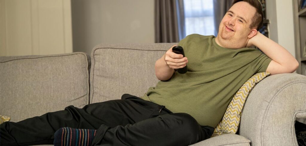 Ein Mann auf einer Couch mit einer Fernbedienung in der Hand. (c) AdobeStock