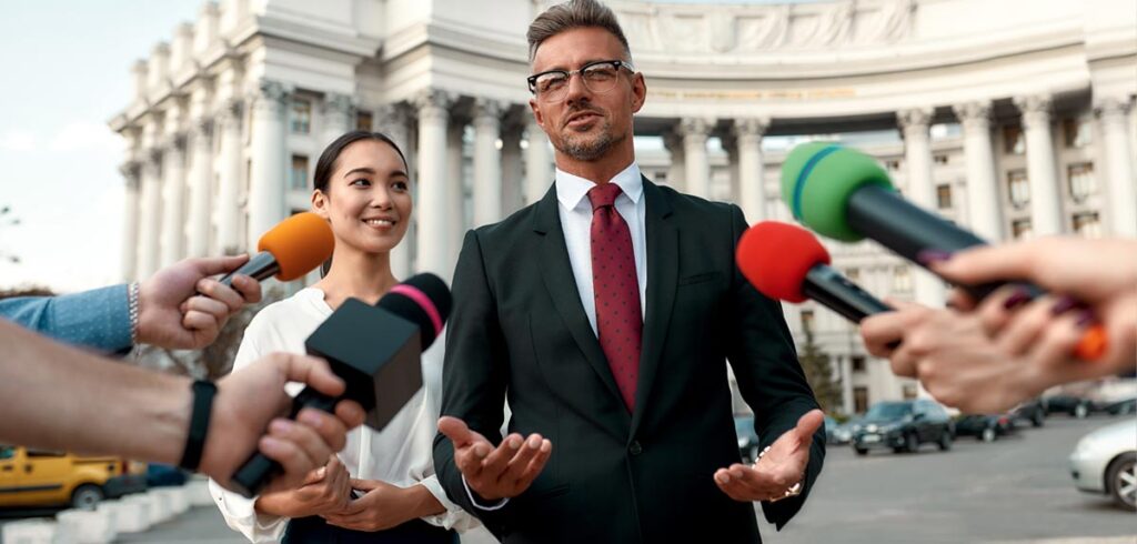 Ein Politiker vor einem Amtsgebäude bei einem Interview. (c) AdobeStock