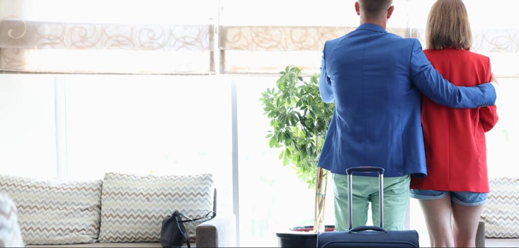 Ein Mann und eine Frau schauen in einer Flughafen Lounge beim Fenster raus. (c) AdobeStock