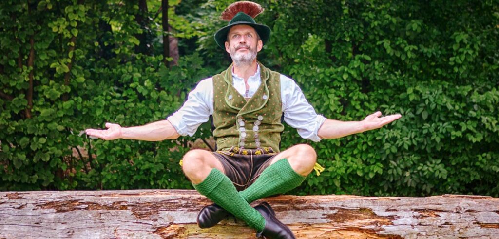 Ein Mann in Tracht beim Meditieren auf einem Baumstamm. (c) AdobeStock