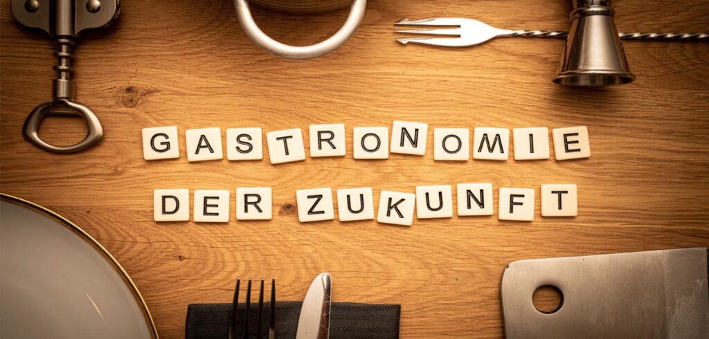 „Finden kein Personal“ – erstes »Bring-Your-Own-Food« Restaurant in Tirol eröffnet Ein Tisch mit dem Schriftzug mit Scrabble-Steinen: "Gastronomie der Zukunft"; darum herum Besteck und Servietten. (c) AdobeStock