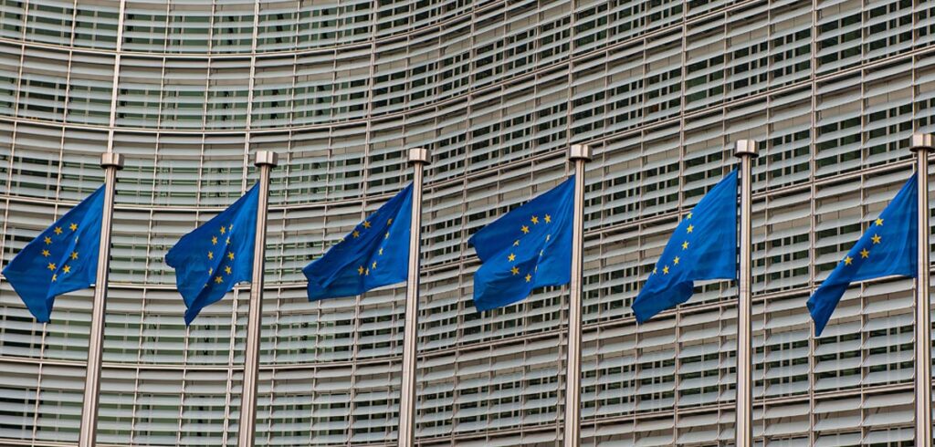 Bürogebäude mit EU-Fahnen im Vordergrund. (c) AdobeStock