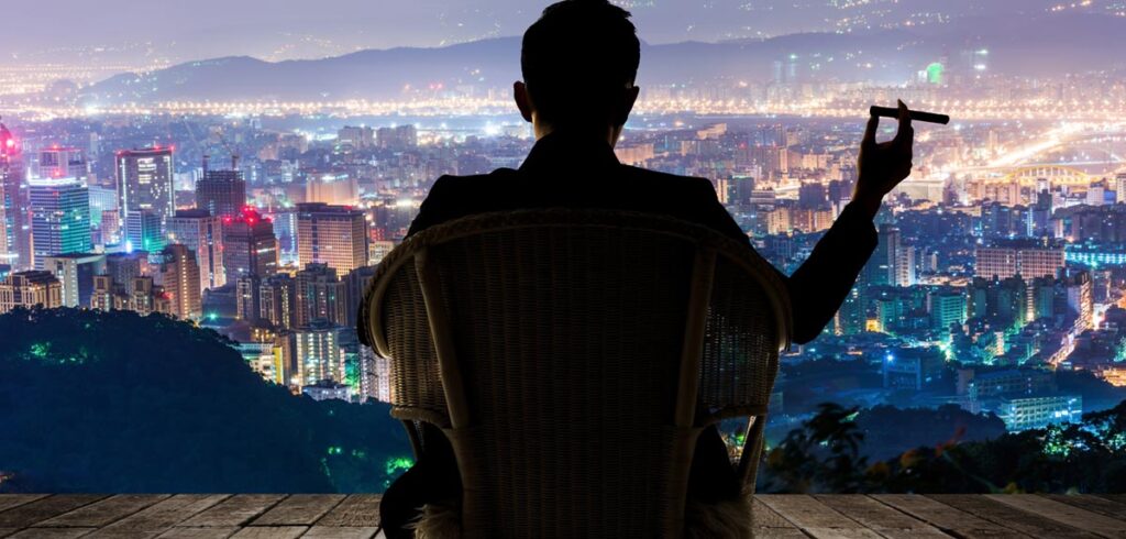 Kontur eines Mannes, der mit einer Zigarre in der Hand auf einer Terrasse sitzt und auf die Skyline einer Stadt schaut. (c) AdobeStock