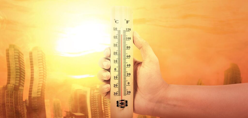 Die Hand eines Mannes, der ein Thermometer hält. Dahinter die Skyline in einer glühend heißen Stadt. (c) AdobeStock
