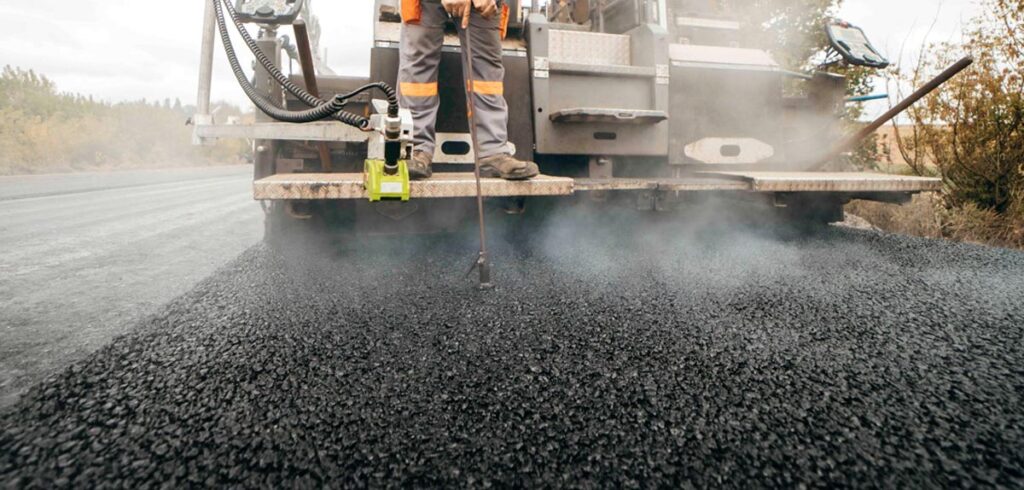Ein Mann auf einer Asphaltiermaschiene bei der Arbeit. (c) AdobeStock