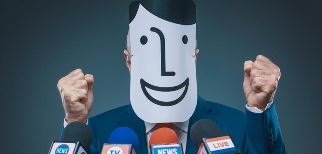 Ein Mann mit erhobenen Fäusten bei einer Rede; sein Gesicht mit einer lachenden Maske verdeckt. (c) AdobeStock