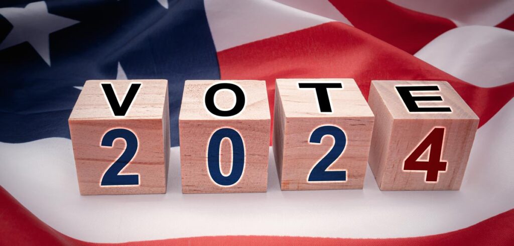 Vote 2024 mit Scrabbel-Würfel auf einer Amerikanischen Flagge. (c) AdobeStock