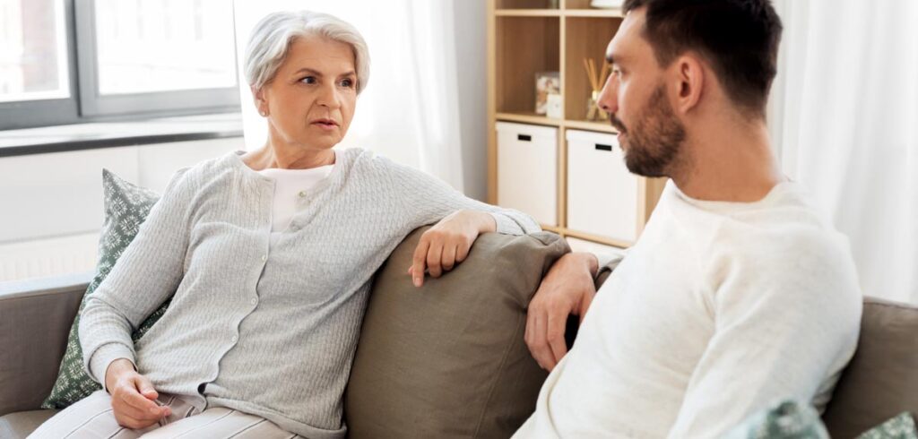 Eine ältere Frau und ein Mann beim Gespräch auf einer Couch. (c) AdobeStock