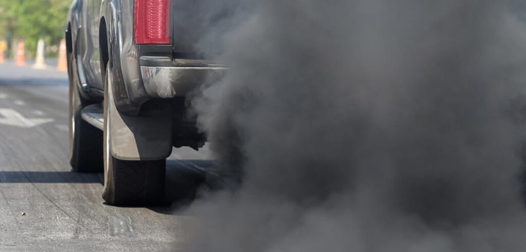 Ein Auto von hinten, das schwarze Abgaswolken ausstößt. (c) AdobeStock
