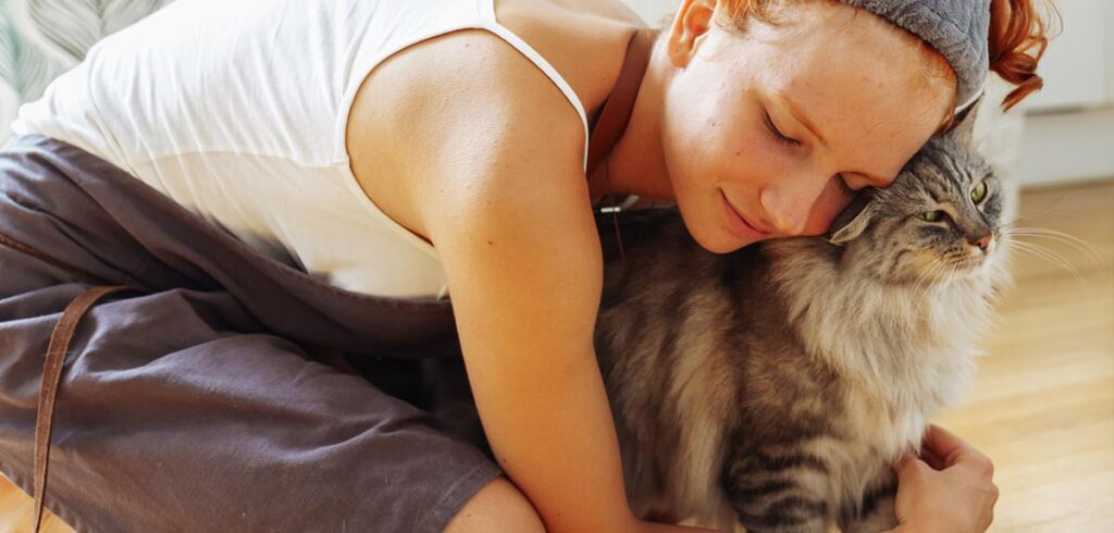 Eine Frau auf dem Boden knieend, die eine Katze innig umarmt. (c) AdobeStock