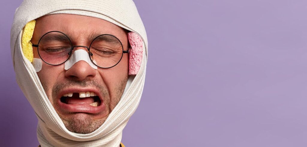 Ein Mann mit dickem Kopfverband, Brille und ausgeschlagenem Zahn. (c) AdobeStock