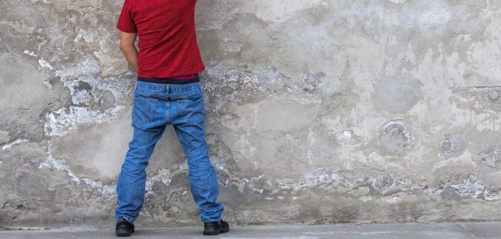 Ein Mann, der gegen eine Wand uriniert. (c) AdobeStock