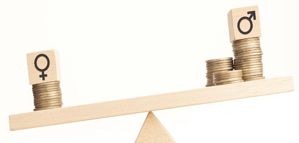 Eine kleine Waage aus Holz; links ein paar Münzen, darauf ein Zeichen für Frau; rechtes mehr Münzen, darauf ein Zeichen für Mann, Stichwort Genderpaygap. (c) AdobeStock