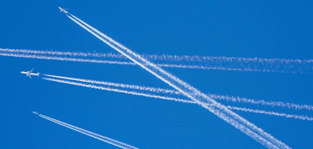 2 Flugzeuge und zahlreiche Kondensstreifen am Himmel. (c) AdobeStock)