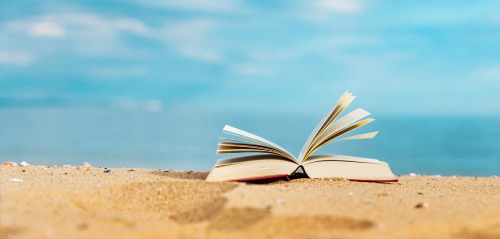 Ein offenes Buch auf einem Sandstrand. (c) AdobeStock