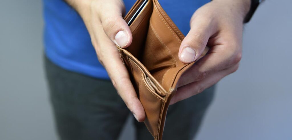 Die Hände eines Mannes, der ein leeres Geldbörsel ohne Geld zeigt. (c) AdobeStock