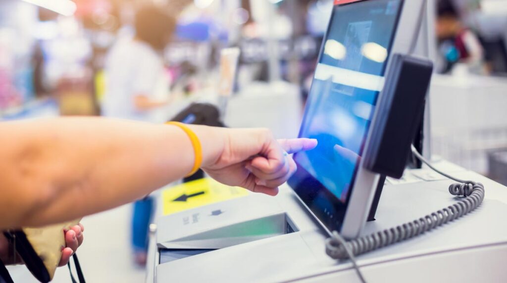 Die Hand einer Frau, die auf eine Selfservice-Kassa in einem Supermarkt zeigt.
(c) AdobeStock