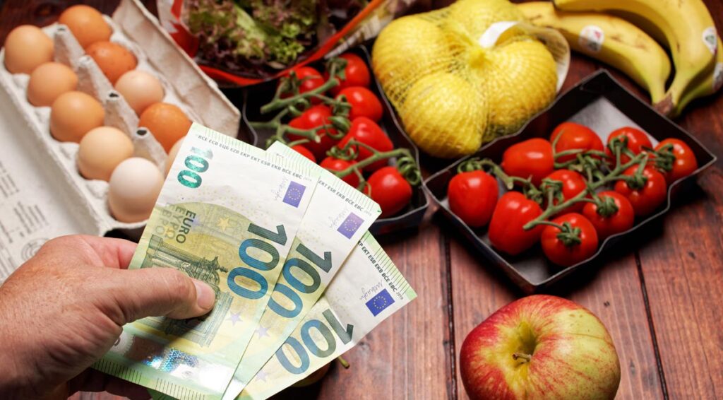 Obst, Gemüse, Eier und die Hand eines Mannes, der 3 Hundert-Euro-Scheine davor hält.
(c) AdobeStock