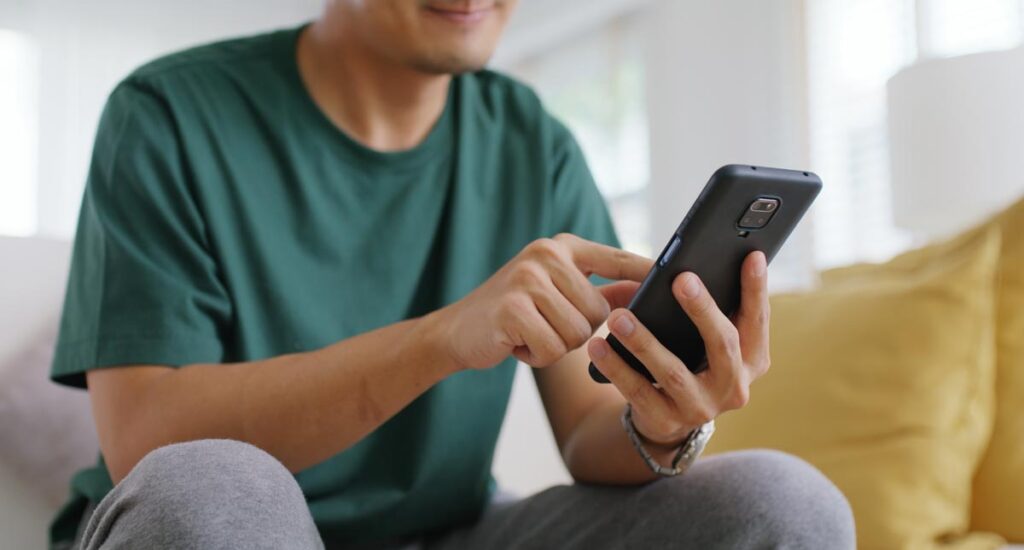 Ein Mann auf der Couch mit einem Handy, Stichwort Wahlzettel 2.0.
(c) AdobeStock