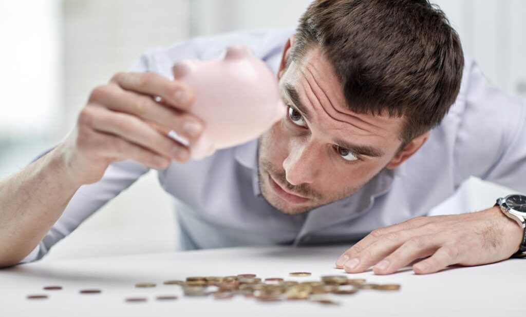 Ein Mann, der verzweifelt sein Sparschwein leert, Stichwort Inflation.
(c) AdobeStock