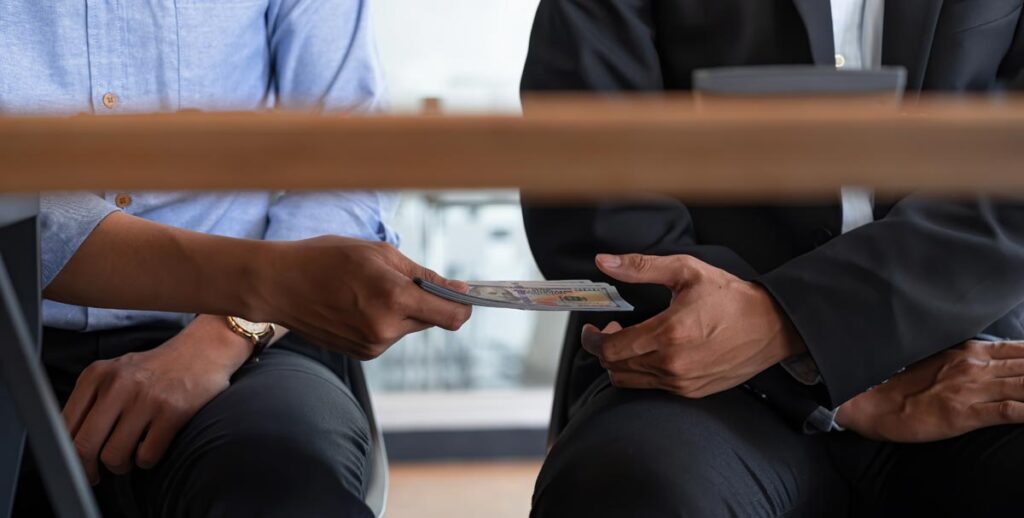 Die Hände zweier Manager, die sich unter dem Tisch Geld geben, Stichwort Leistungsträger.
(c) AdobeStock