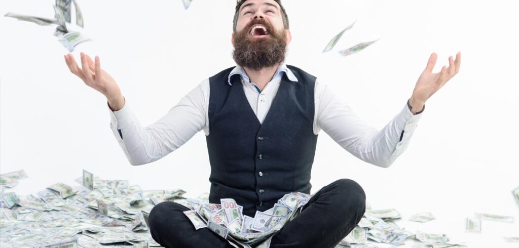 Ein Mann sitze im Schneidersitz auf dem Boden und wirft Geldscheine in die Luft. (c) AdobeStock